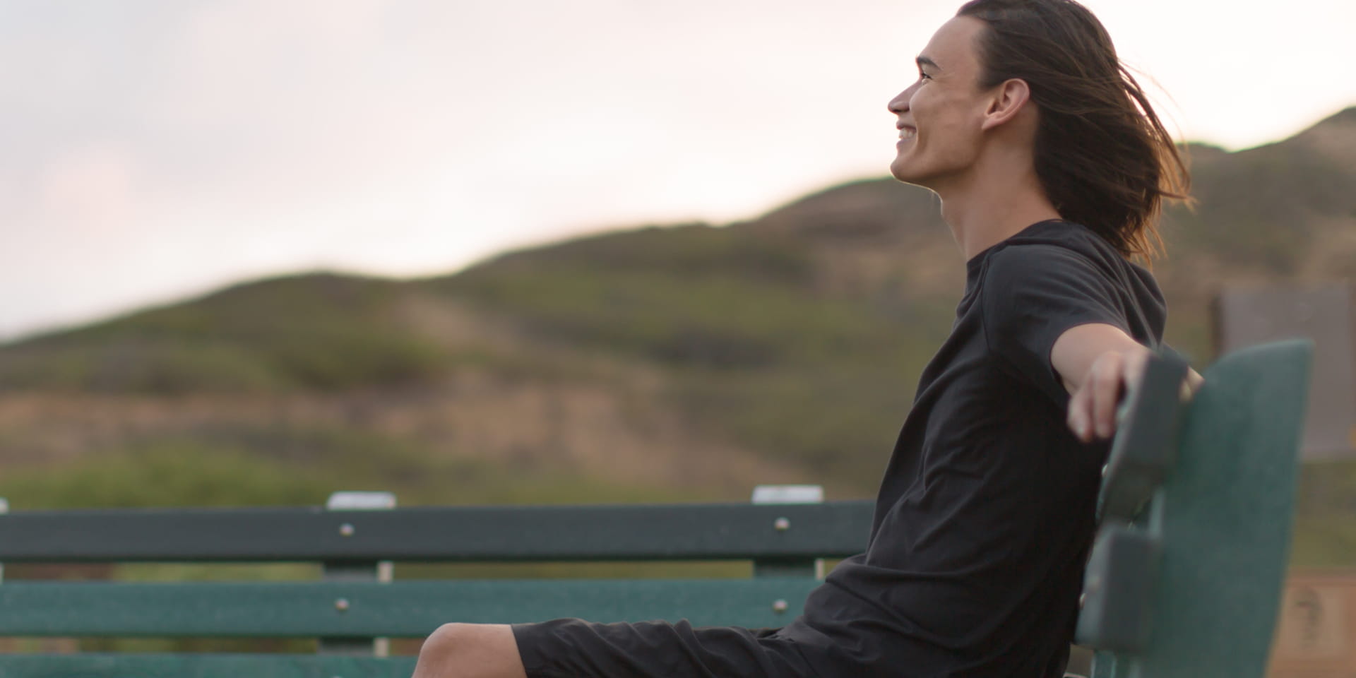 Young man looking happy and relaxed as he sits on a bench taking in nature. 